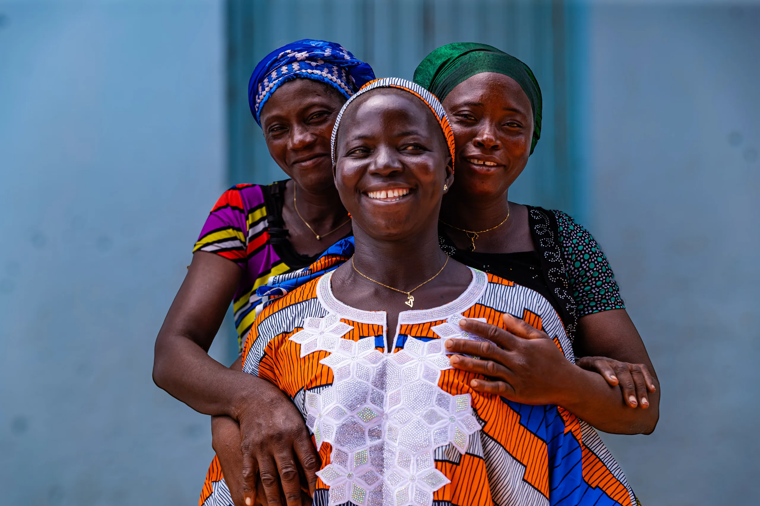 Three women in headscarves, smiling, arm in arm