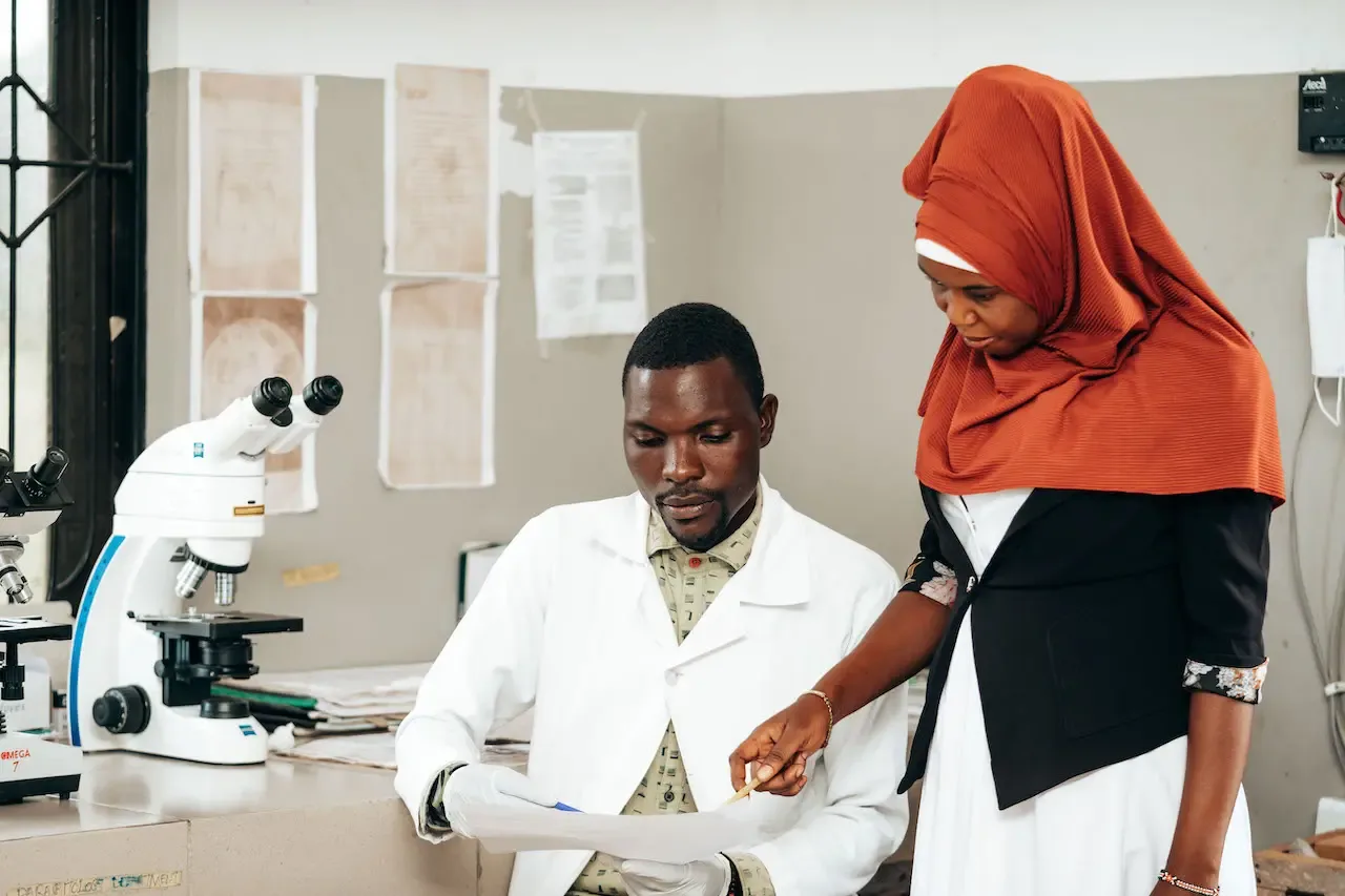 A laboratory technician at a microscope with a colleague