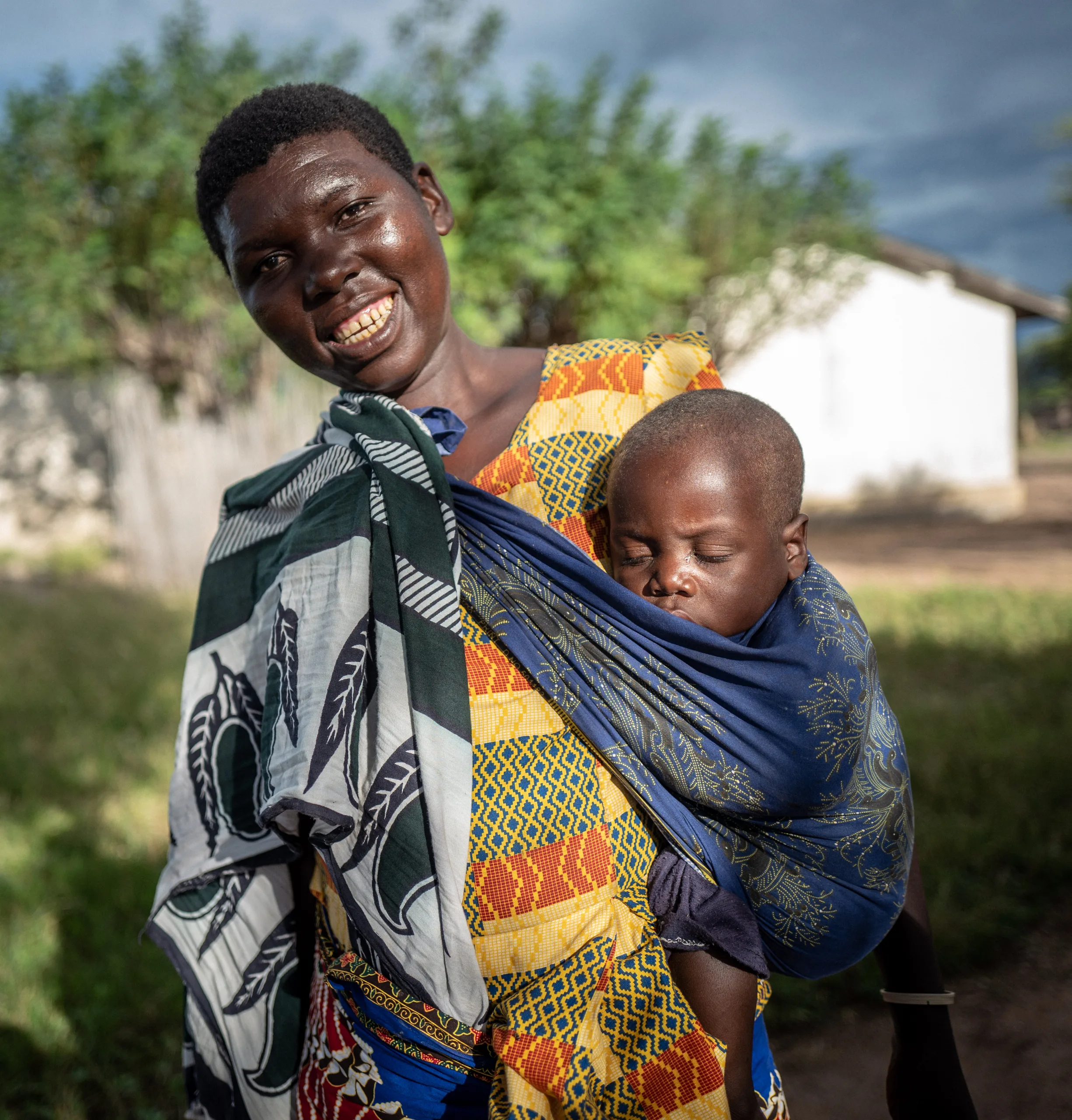 A smiling woman carrying her baby on her back